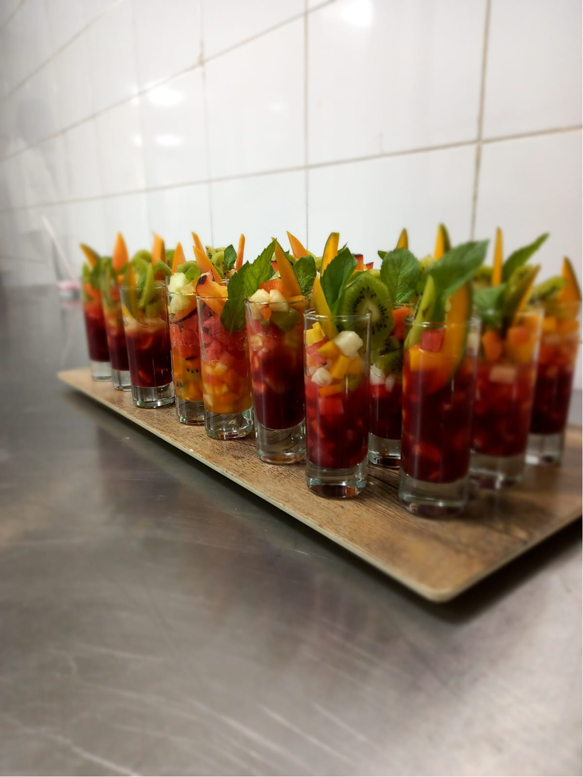 Fresh fruit cups layered in tall glasses with mint and colorful garnish.