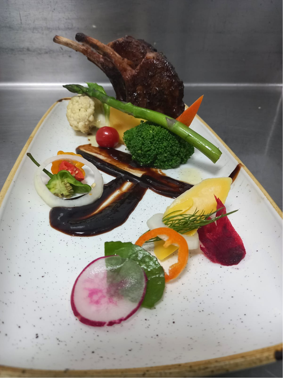 Plated lamb chops with asparagus, vegetables, and glossy reduction.