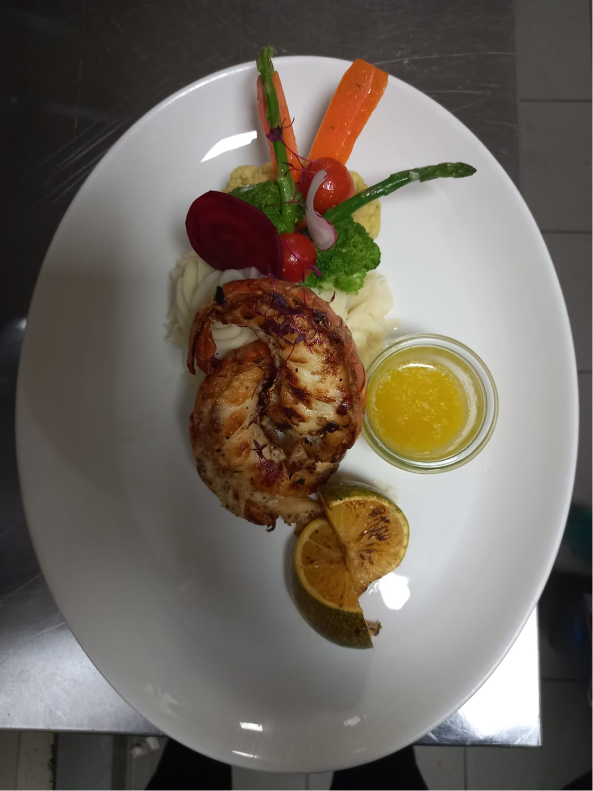 Grilled lobster plated with mashed potato, vegetables, and citrus butter.